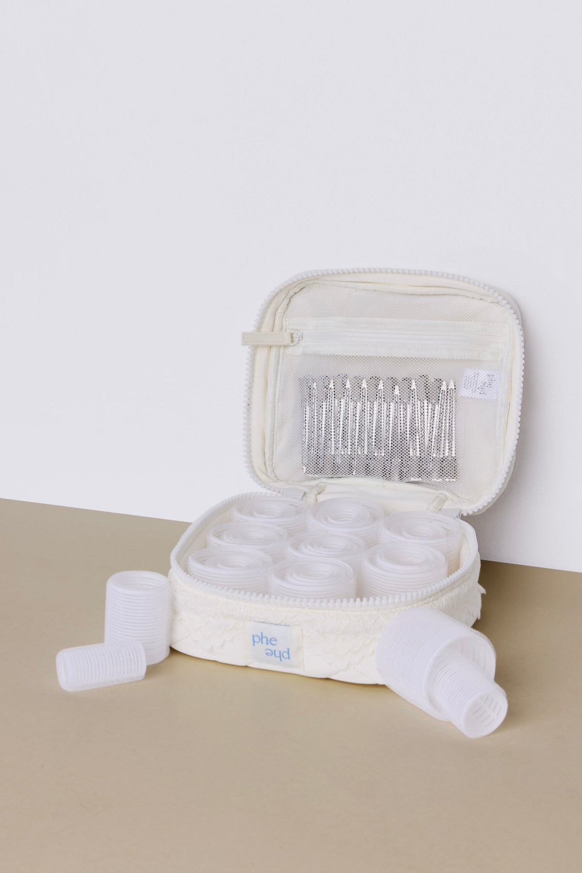 The phe phe Hair Roller Set Pearl features an open, lace-textured zipper case containing several white velcro rollers and a mesh pocket filled with silver curl-setting clips.
