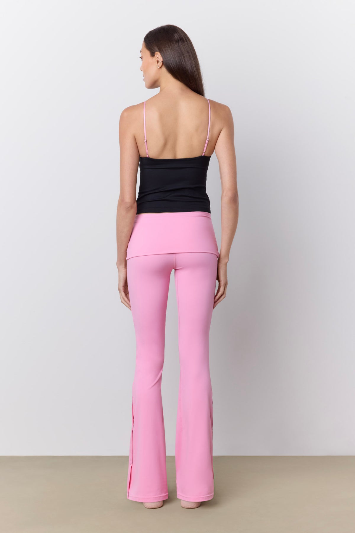 A woman shown from the back wearing bright pink flared pants and a black camisole top against a plain light gray studio background.