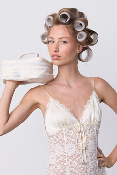 A woman with phe phe Hair Roller Set Pearl velcro rollers in her hair holds a small, cream-colored vanity case on her shoulder.