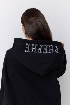 A person shown from behind wearing a black hoodie with the word 'PHEPHE' spelled out in sparkling silver rhinestones across the back of the hood, against a plain light gray background.