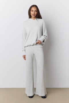 A woman modeling a light gray two-piece loungewear set consisting of a waffle knit long-sleeve hoodie and matching wide-leg pants, standing against a neutral studio background.