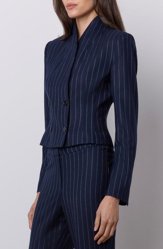 A woman modeling a navy blue pinstripe two-piece suit with a double breasted blazer and matching wide-leg trousers, standing against a neutral studio backdrop.