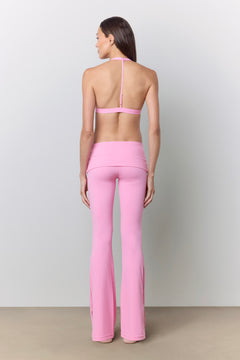 A woman shown from the back wearing a pink halter-style sports bra and matching pink high-waisted flared leggings, standing against a plain light gray studio wall.