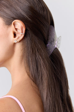 A close-up side profile of a woman with long dark brown hair wearing a translucent opal hair claw clip with small silver rhinestones. The brand name 'phe phe' is printed on the clip.