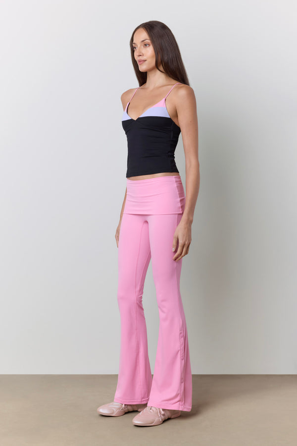 A woman modeling a pair of bright pink high-waisted flared pants, paired with a black camisole and light pink shoes, against a neutral studio background. |M1