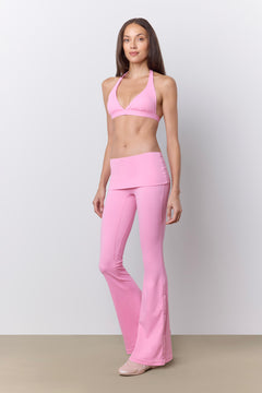 A woman modeling a light pink activewear set consisting of a halter-neck sports bra and matching high-waisted flared leggings, standing against a neutral studio backdrop.