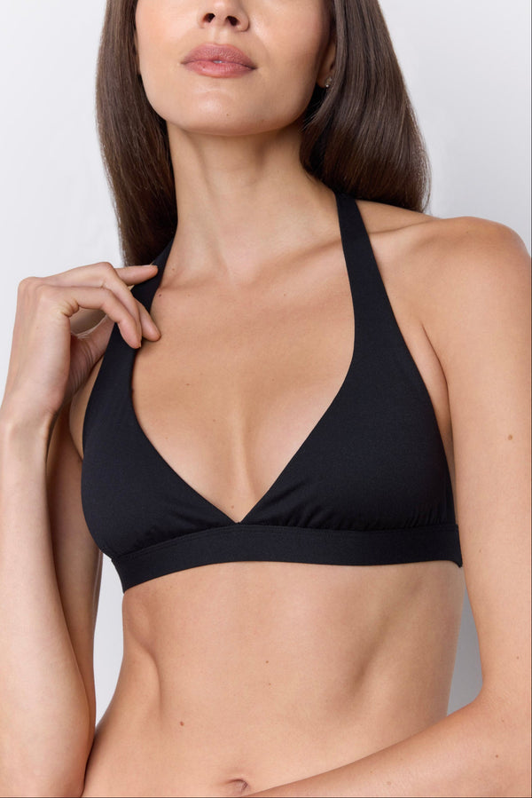 A close-up of a woman wearing a black halter-style bikini top against a light gray studio background. |M1