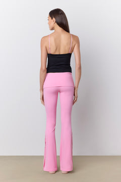 A woman shown from the back wearing bright pink flared pants and a black camisole top against a plain light gray studio background.