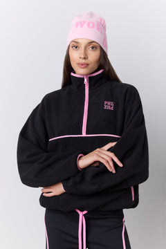 A model wearing a black quarter-zip fleece jacket with pink piping and a matching pink beanie with 'JUST WORKED OUT' printed on it, posed against a light gray studio background.