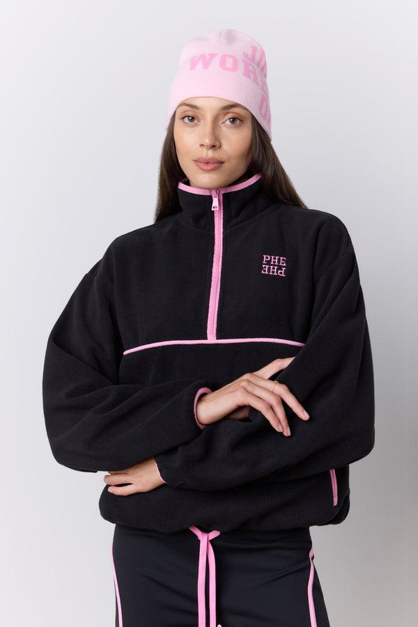 A model wearing a black quarter-zip fleece jacket with pink piping and a matching pink beanie with 'JUST WORKED OUT' printed on it, posed against a light gray studio background. |M1