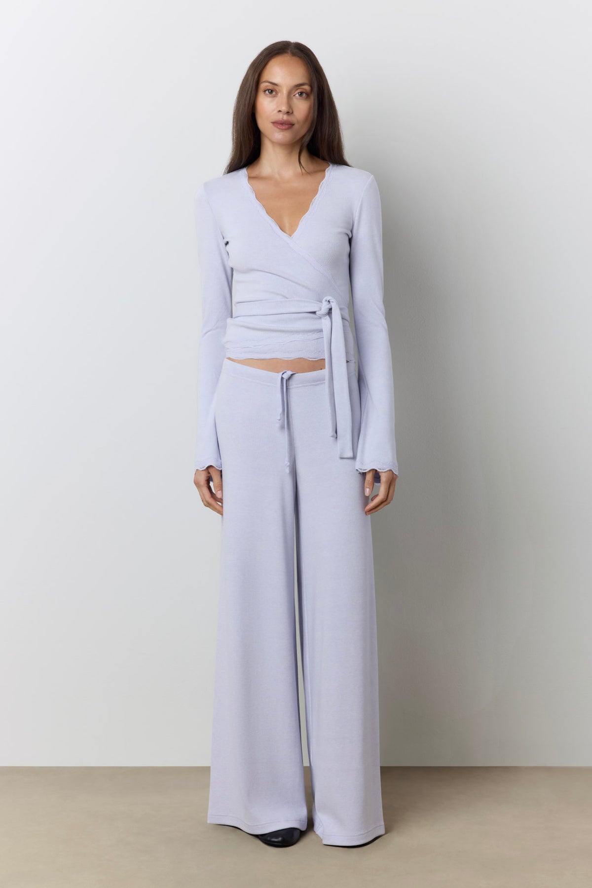 A woman modeling a periwinkle wrap top and matching wide-leg lounge pants against a neutral studio background.