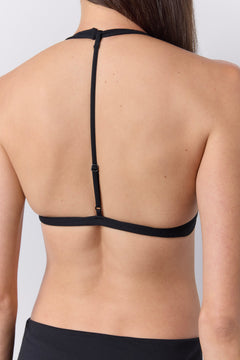 Rear view of a woman wearing a black halter-style sports bra, showing the thin back straps and band against a light gray studio background.