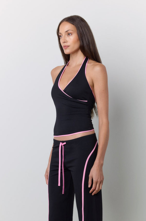 A woman modeling a black halter top and matching wide-leg pants with pink trim and drawstrings, standing against a light gray studio wall. |M1