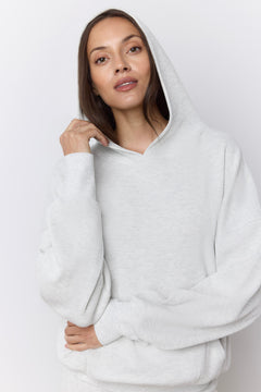 A woman wearing a light gray oversized pullover hoodie with a relaxed fit, photographed against a plain light gray studio background.