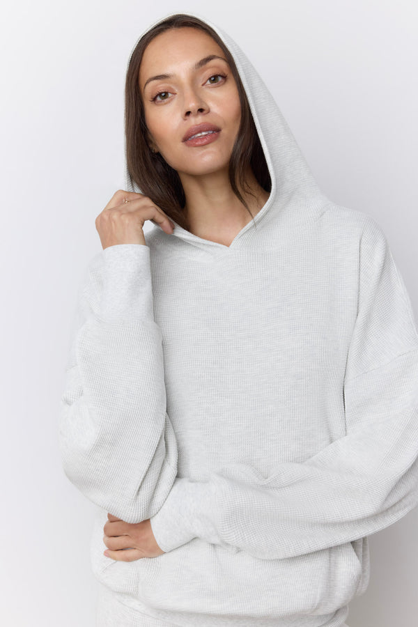 A woman wearing a light gray oversized pullover hoodie with a relaxed fit, photographed against a plain light gray studio background. |M1
