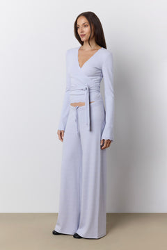 A woman modeling a periwinkle wrap top and matching wide-leg lounge pants against a neutral studio background.