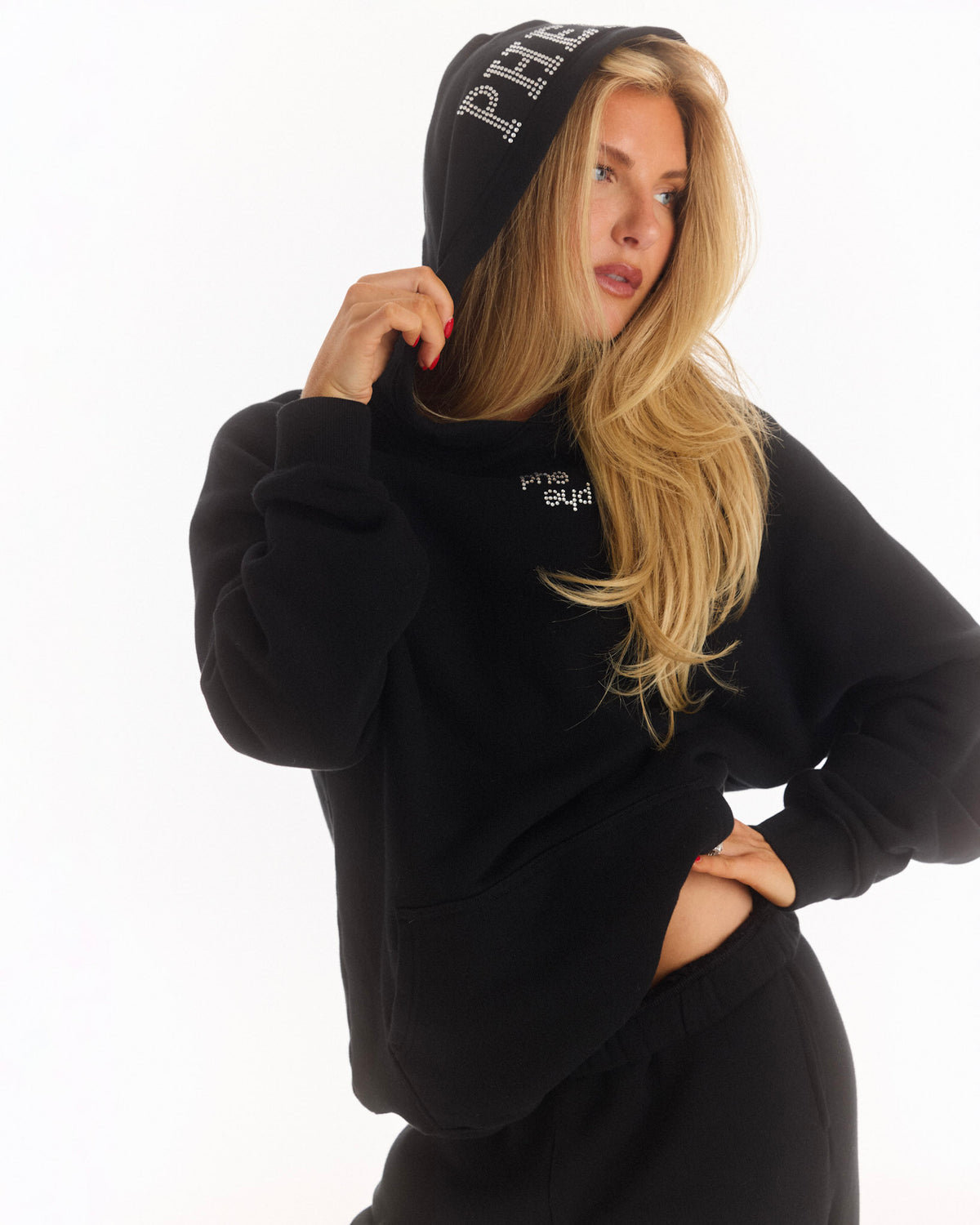 A woman wearing a black hoodie and matching sweatpants with white 'Phe Phe' rhinestone lettering on the hood and chest, posed against a clean white background.